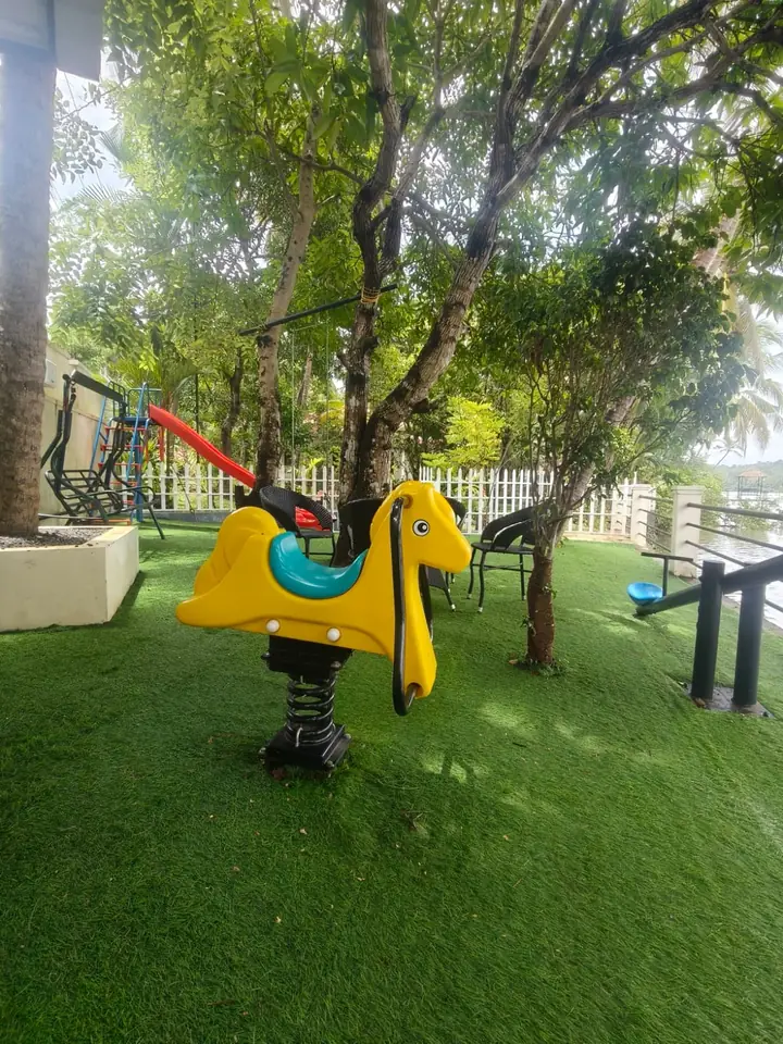 Mini kids park at BelleVue Kozhikode with a slide, swing and spring rider on the lawn under the trees
